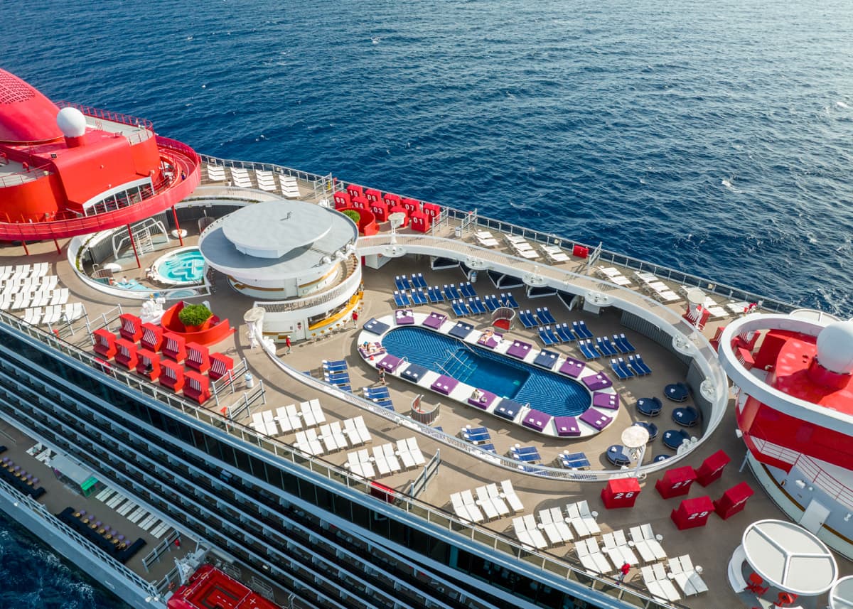 Aerial view of a cruise ship deck featuring a pool, lounge chairs, and red funnels.
