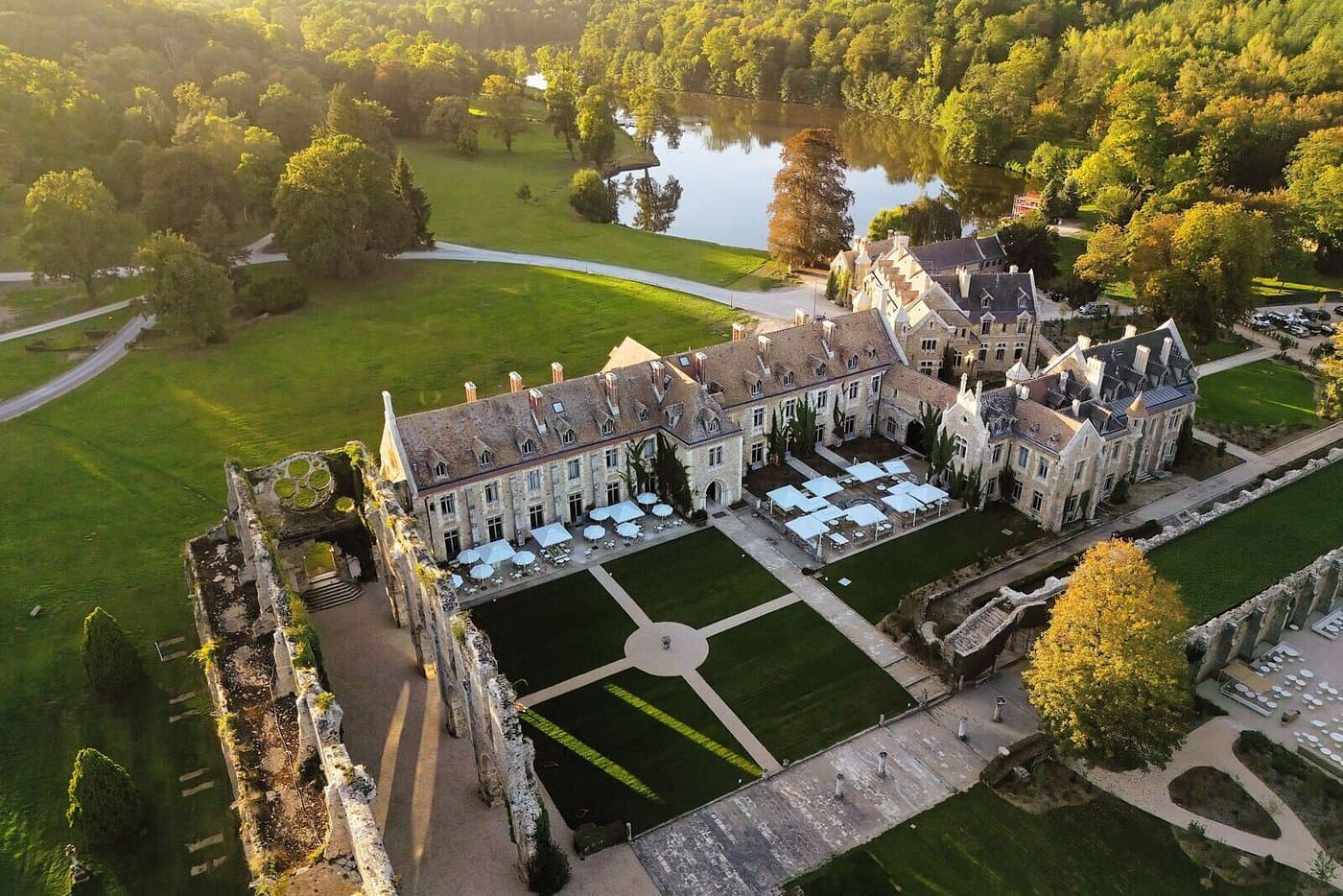 Aerial view of a historic stone estate with ruins, manicured lawns, and a scenic lake.
