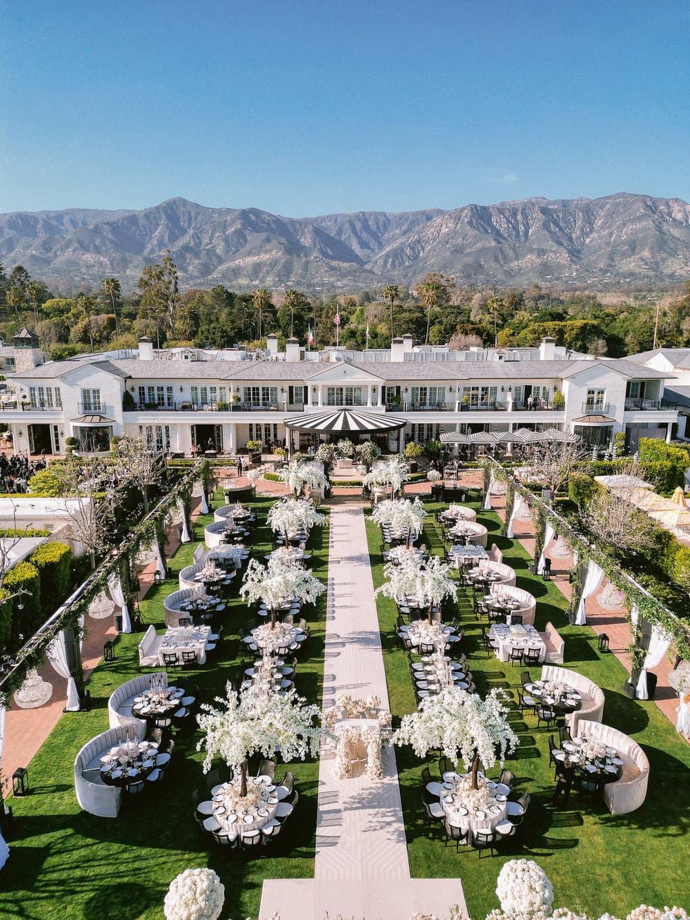 Elegant outdoor wedding reception on a lawn with white flowering trees and mountain views.